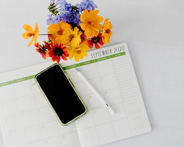 Un smartphone, un agenda papier, un stylo et un bouquet de fleurs.
